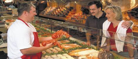 Una exhibición de mariscos con varios productos como langostas y pescado, una persona con delantal rojo y una barrera de vidrio.