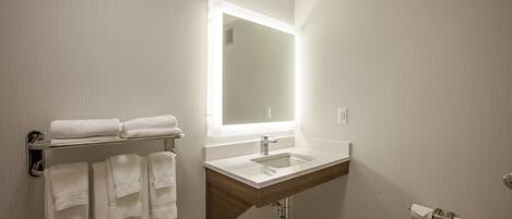 A bathroom with a sink, mirror, towel rack, and toilet paper holder.