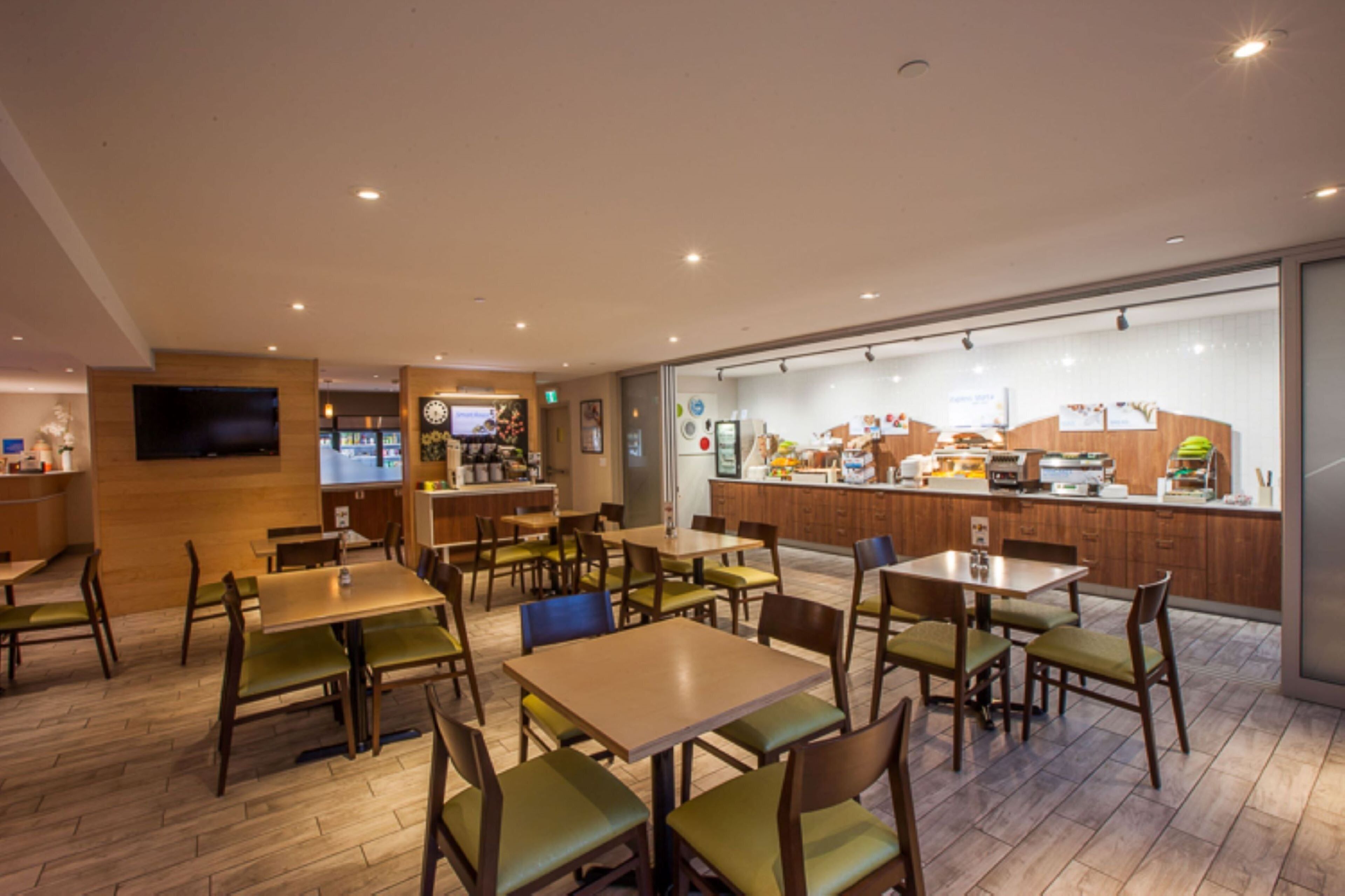Un restaurant avec des tables et des chaises en bois, un comptoir où sont exposés les produits, et un téléviseur fixé au mur.