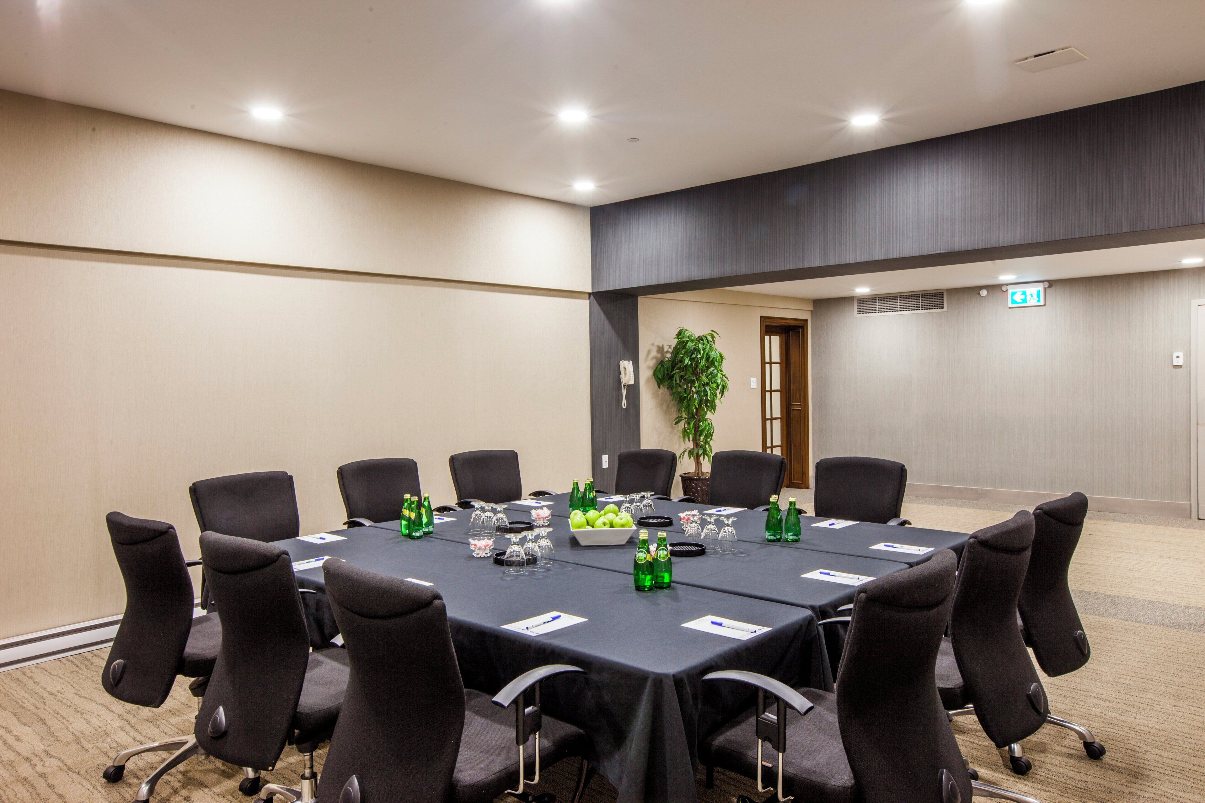 Een congreszaal met een lange tafel, stoelen en diverse voorwerpen, zoals flessen en een schaal met appels.