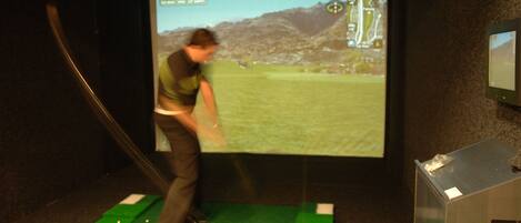 A person playing golf on a mat with a projection screen displaying a golf course in the background.
