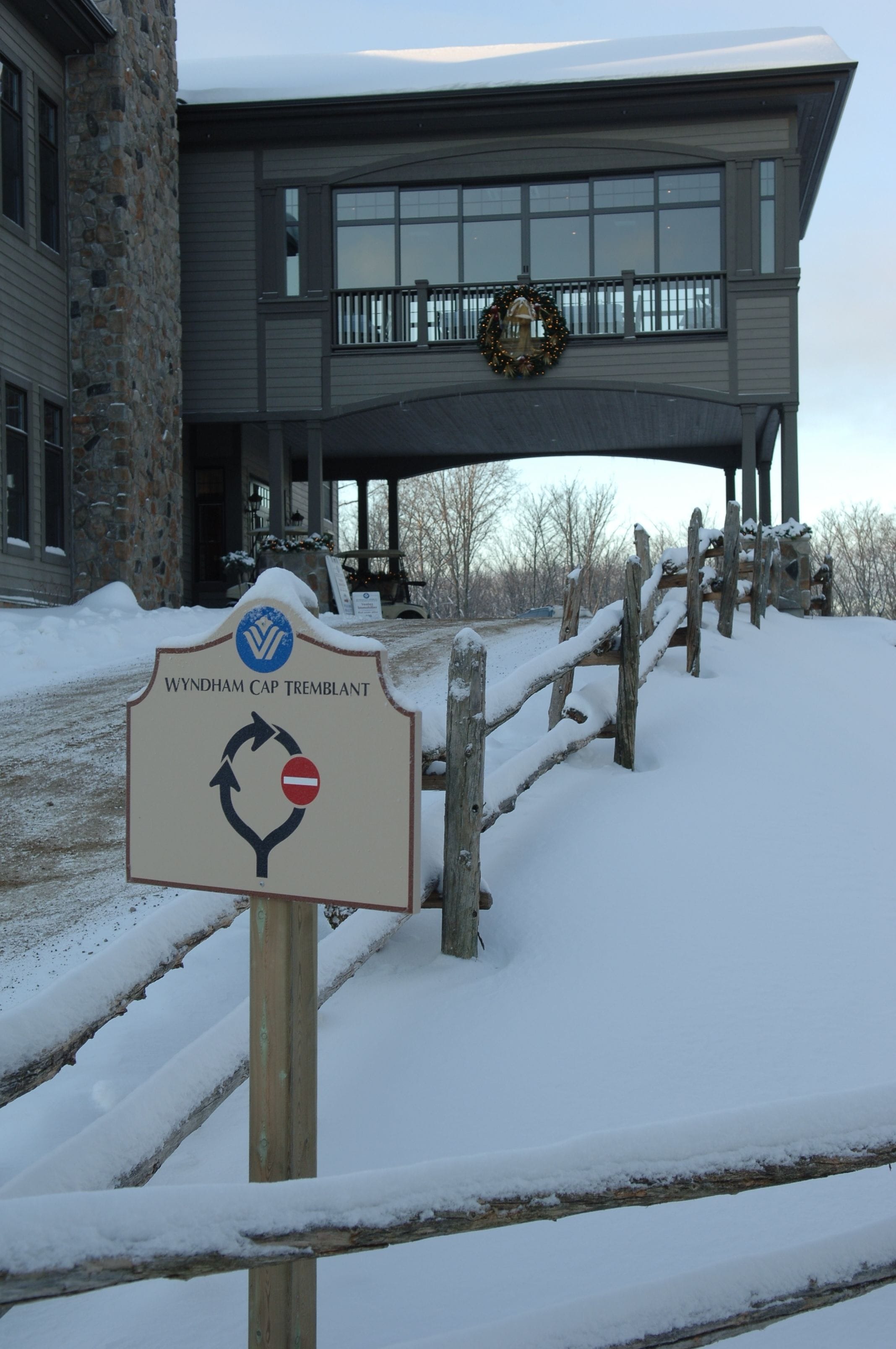 Señal de Wyndham Cap Tremblant con un símbolo de prohibido, un edificio de piedra y una valla de madera al fondo.