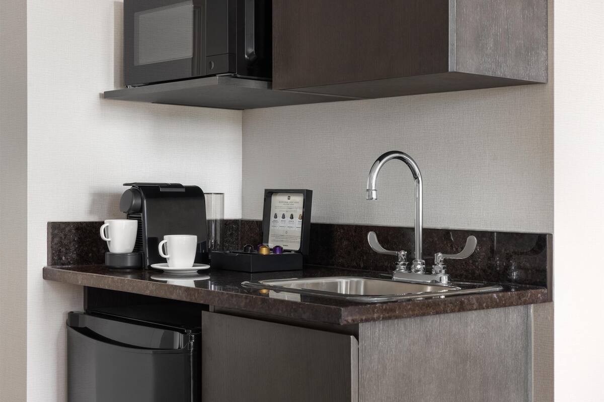 A modern kitchen with a built-in microwave, a coffee machine, and a stainless steel sink.