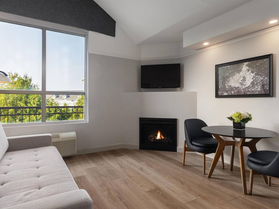 A modern living room with a fireplace, a sofa, a dining table with chairs, and a TV mounted on the wall.