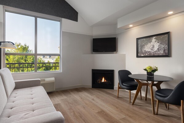 A modern living room with a fireplace, a sofa, a dining table with chairs, and a TV mounted on the wall.