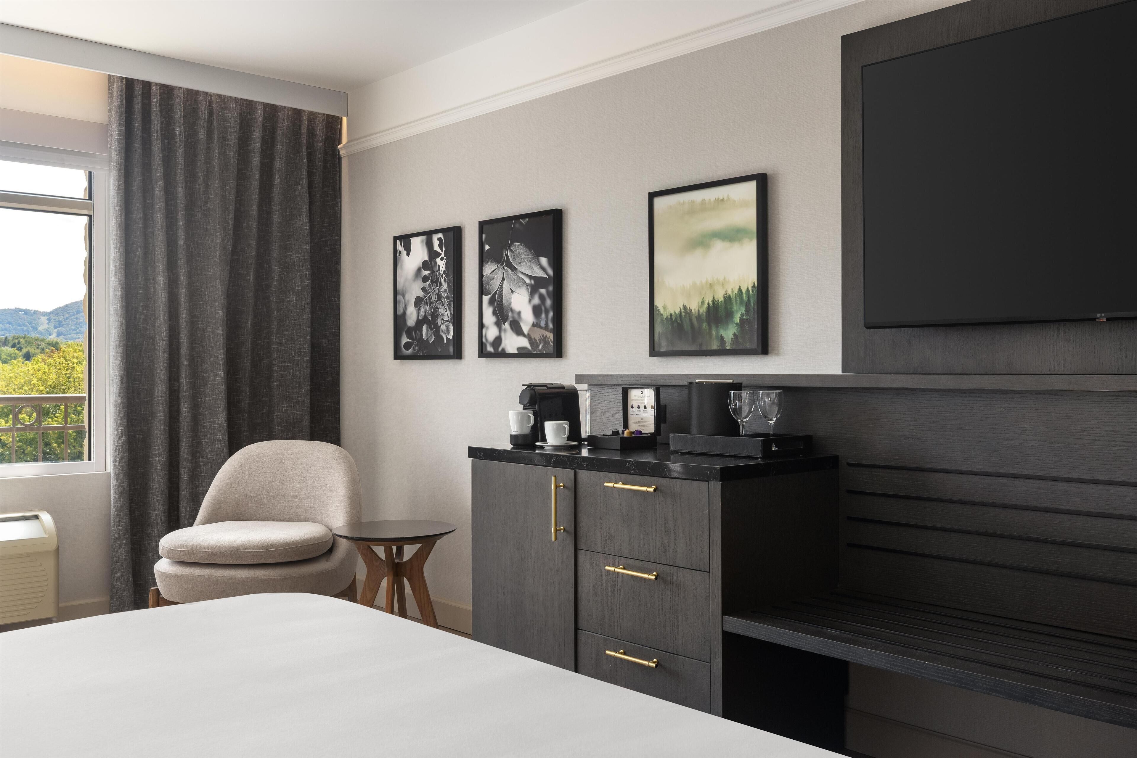 A hotel room with a bed, a chair, a small table, a cabinet, and a TV.
