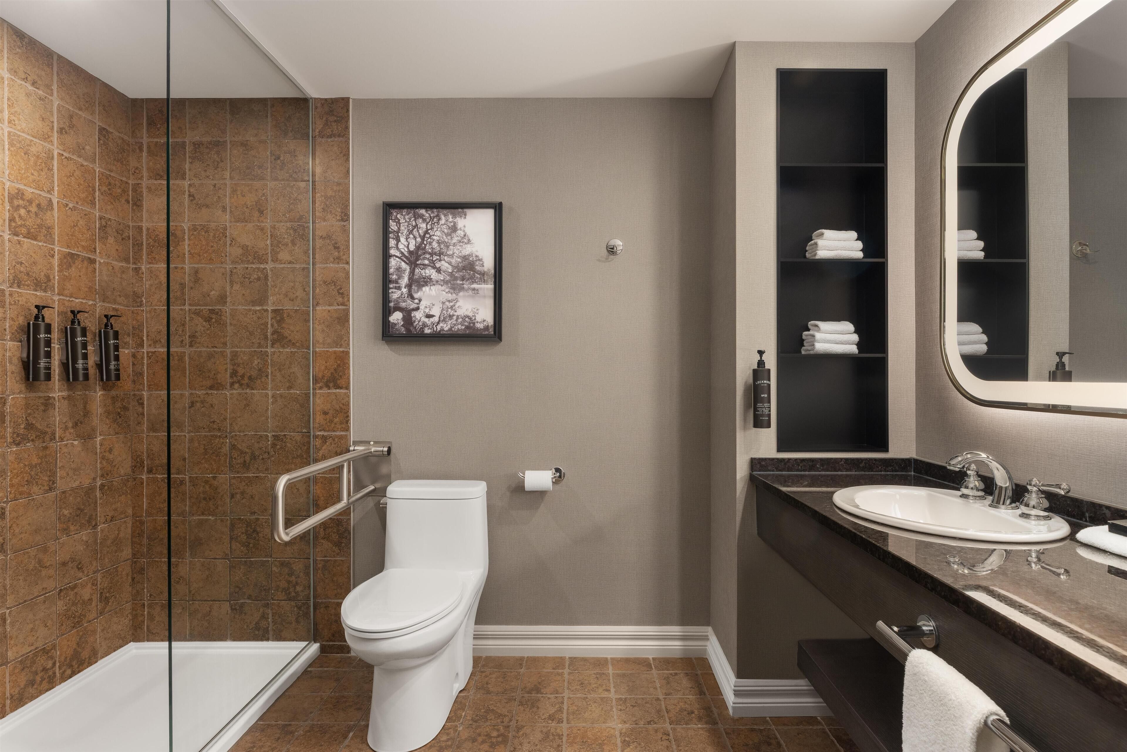 A modern bathroom with a glass shower enclosure, a toilet, a sink with a vanity, and a large mirror.