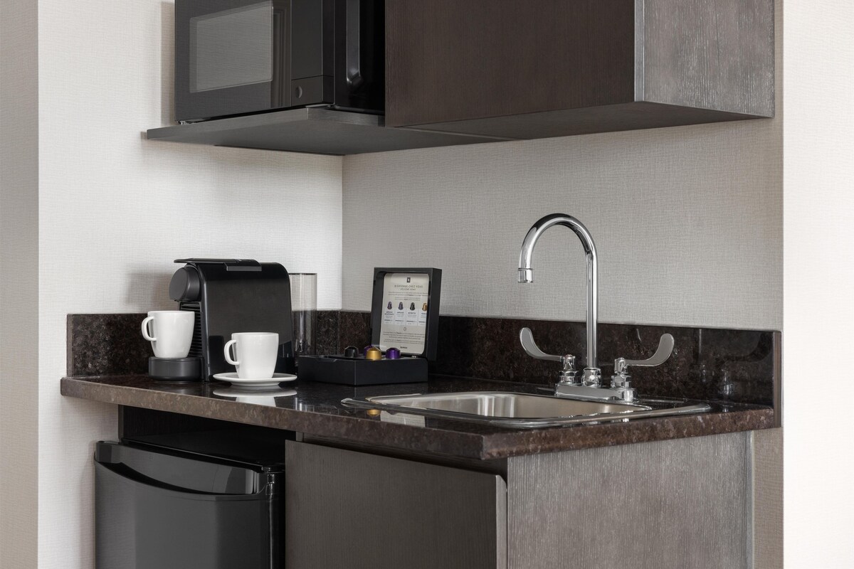 A modern kitchen with a built-in microwave, coffee maker, and stainless steel sink.