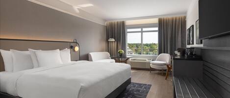 Une chambre d’hôtel moderne, dotée d’un grand lit, d’un bureau, d’une chaise et offrant une vue sur l’extérieur.