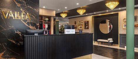 A hotel reception area with a marble wall, a black reception desk, and a chandelier.