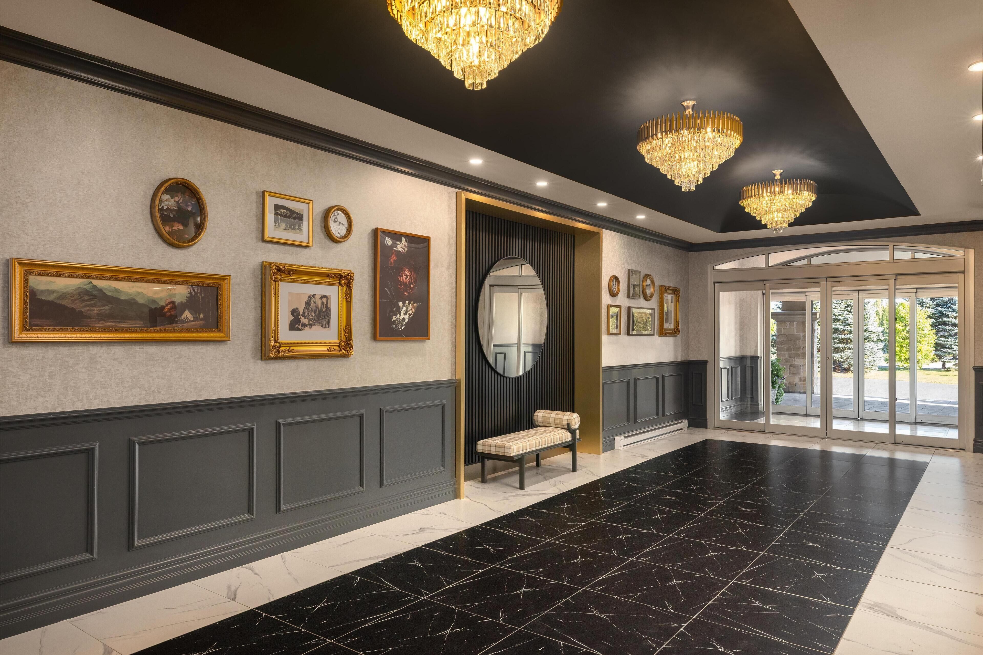 Um hall amplo com piso de mármore preto e branco, um banco e um espelho grande.