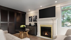 A modern living room with a fireplace, a flat-screen TV mounted above it, and a dining area with a round table and chairs. - Hotel Vallea Bromont, Tapestry Collection by Hilton (Bromont)