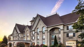 A large, multi-story hotel with a classic architectural style, featuring a prominent entrance with a sign that reads "Vallea Hotel & Suites." - Hotel Vallea Bromont, Tapestry Collection by Hilton (Bromont)