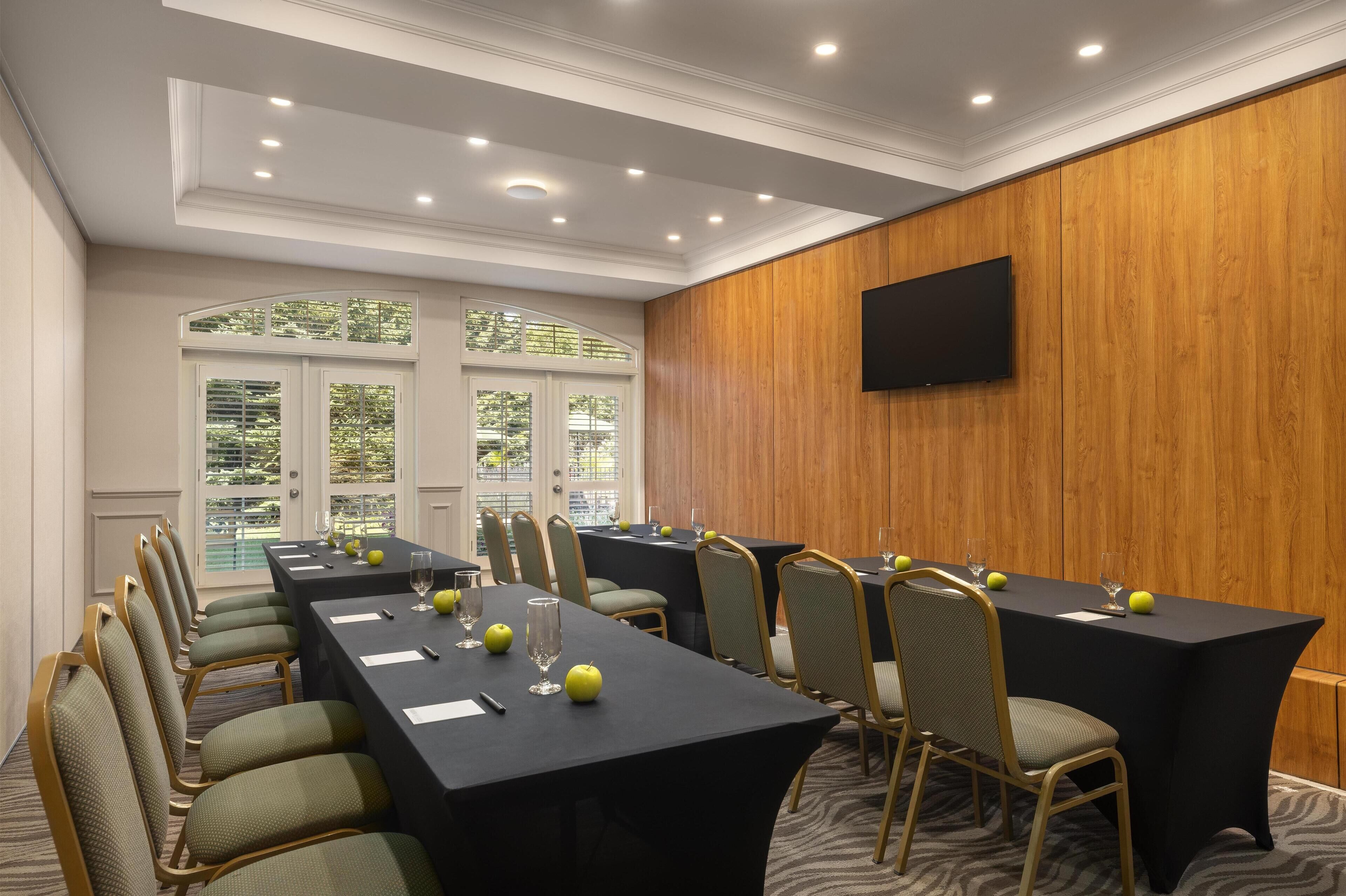 Un salón de conferencias con mesas largas, sillas y un televisor de pantalla plana en la pared.