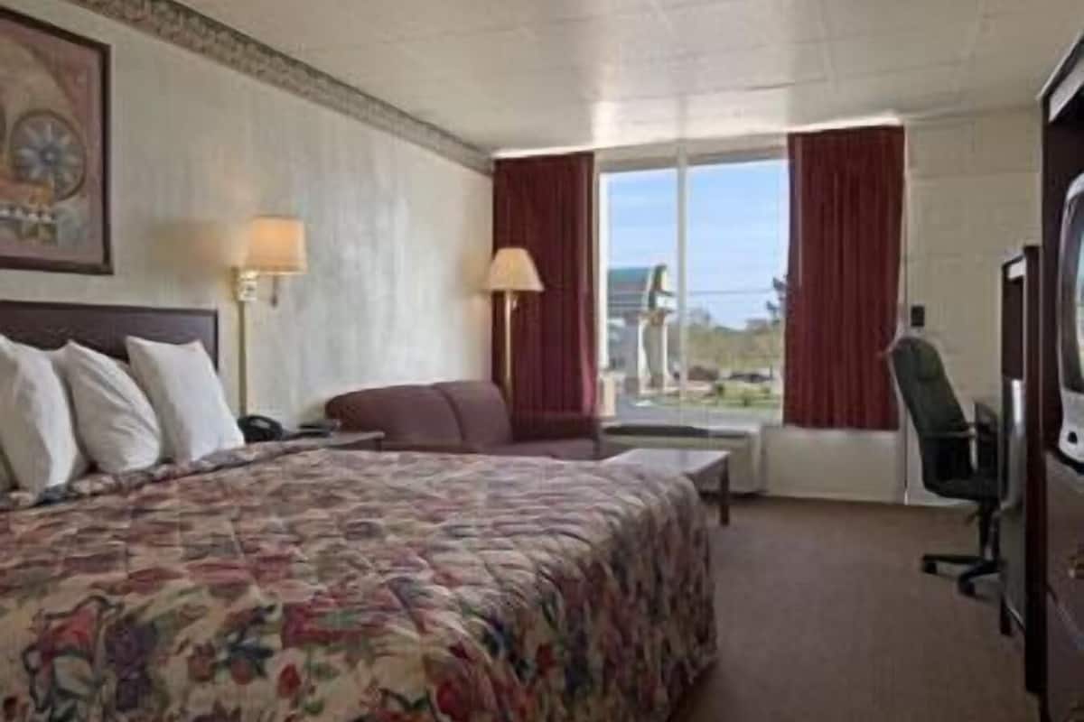 Ett hotellrum med en säng, ett skrivbord, en stol och ett fönster med gardiner.