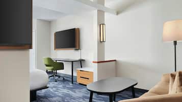 A hotel room with a bed, a desk, a chair, a TV, and a lamp.