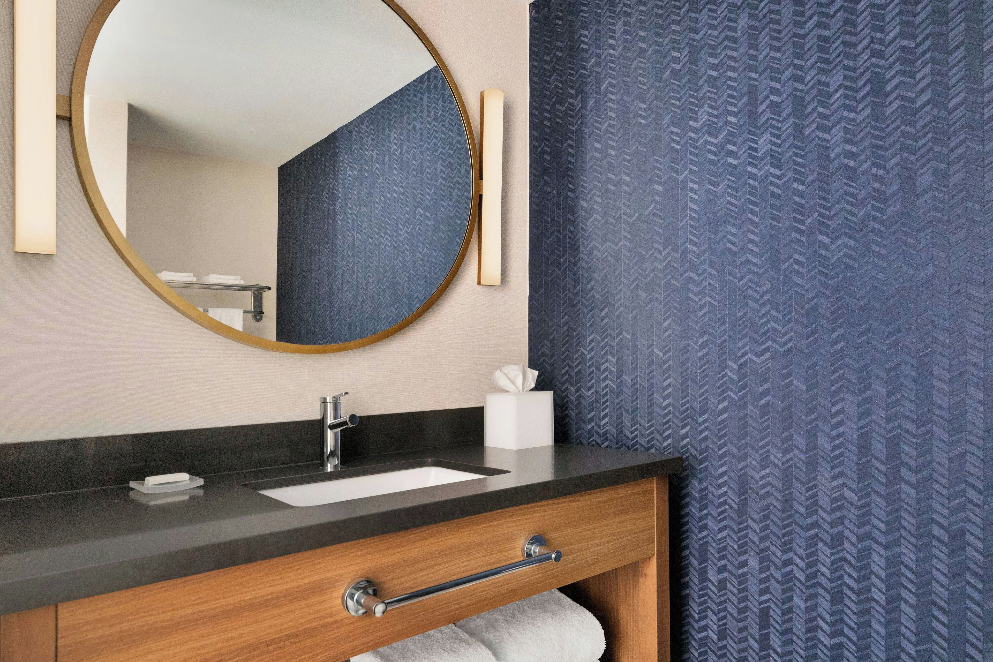 A bathroom with a round mirror, a sink, a towel rack, and a towel on the floor.