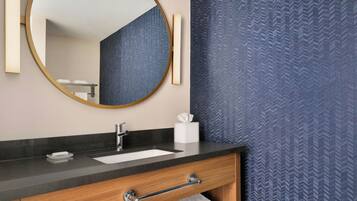A bathroom with a round mirror, a sink, a towel rack, and a towel on the floor.