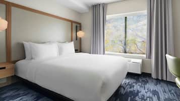A hotel room with a large bed, a nightstand, a lamp, a window with curtains, and a radiator.