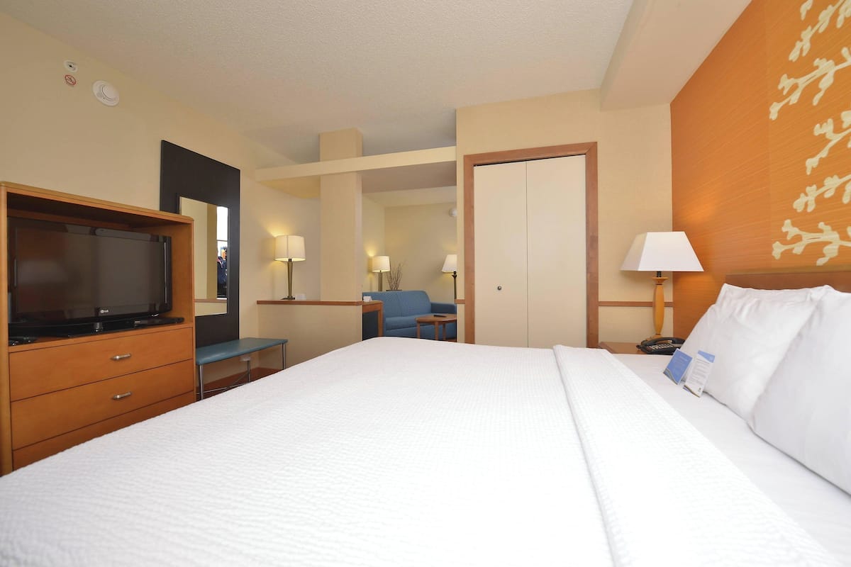 A hotel room with a large bed, a television, a desk with a chair, a mirror, and a door.