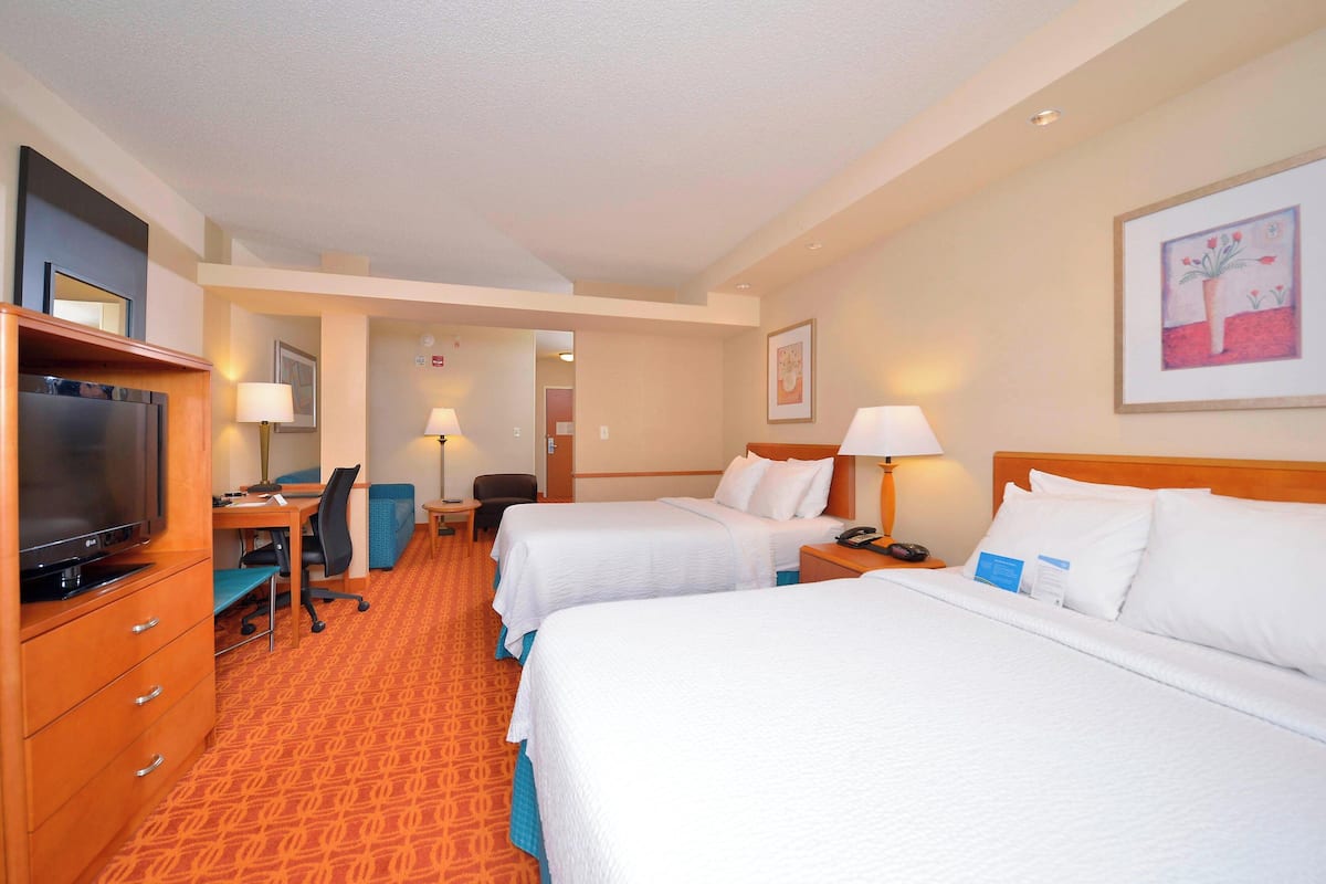A hotel room with two beds, a desk with a chair, a television, and a desk lamp.