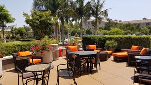 An outdoor patio area with wicker furniture, orange cushions, and potted plants. - Hilton Garden Inn Oxnard/Camarillo (Oxnard)