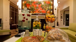 A buffet setup with a fruit display, a beverage dispenser, and a covered dessert station. - Hilton Garden Inn Oxnard/Camarillo (Oxnard)