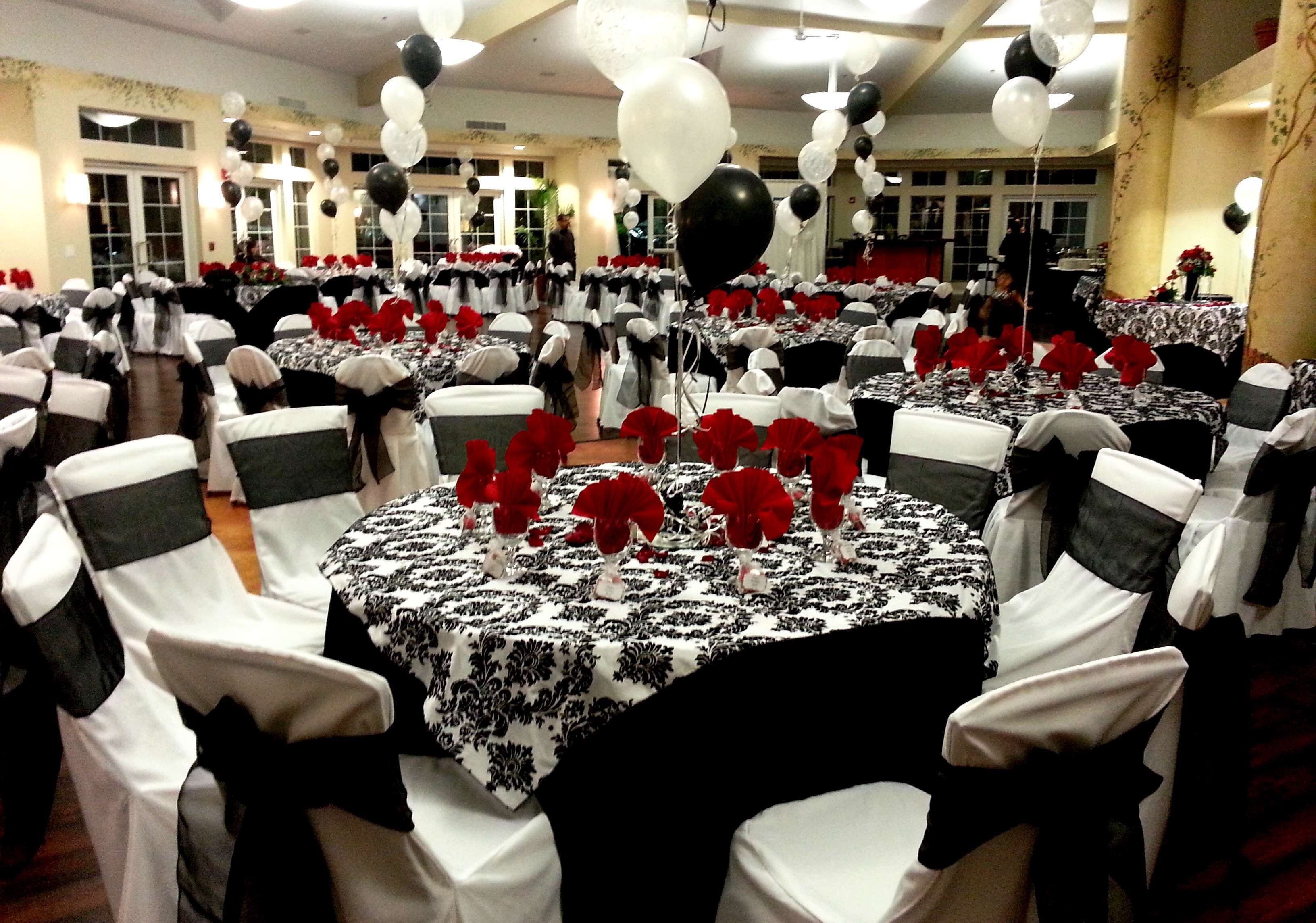 Une salle de banquet avec des tables rondes, des nappes blanches et noires, et des fleurs rouges.