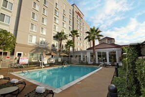 A hotel with a swimming pool, outdoor seating, and palm trees. - Hilton Garden Inn Oxnard/Camarillo (Oxnard)
