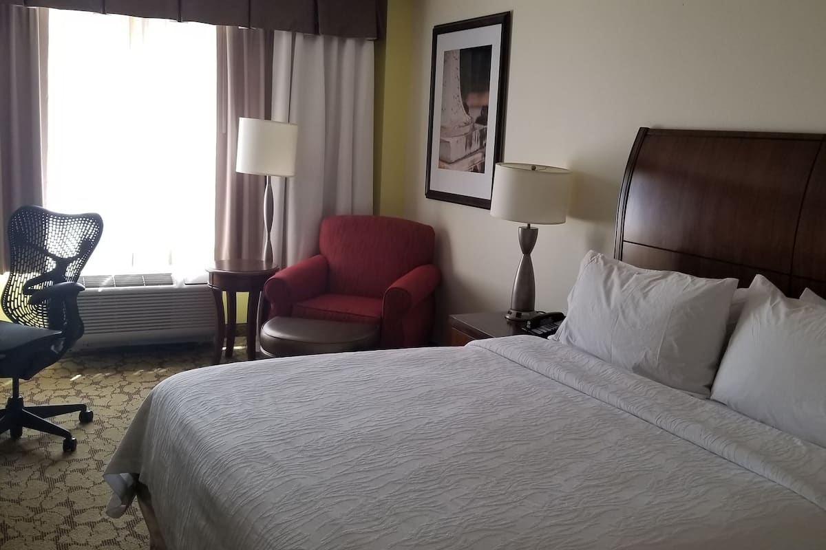 Une chambre d’hôtel avec un grand lit, un fauteuil rouge, un bureau avec une lampe et une chaise.