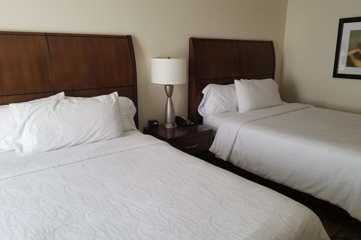 Une chambre d’hôtel avec deux lits, chacun doté de draps blancs et d’une tête de lit en bois. On y trouve une table de chevet avec une lampe et un téléphone.