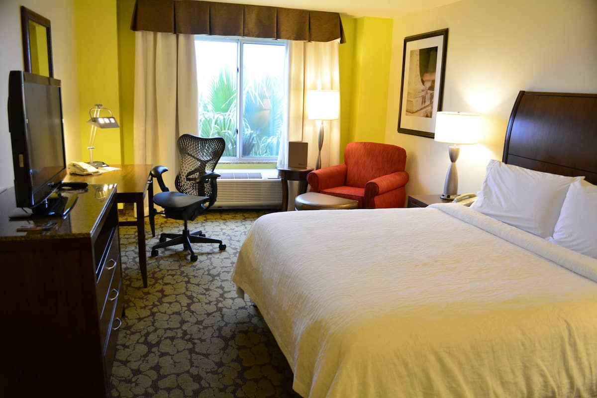 Une chambre d’hôtel avec un lit, un bureau avec un ordinateur, une chaise, une télévision et une fenêtre avec des rideaux.