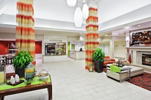 A spacious hotel lobby with a dining area, a fireplace, and a kitchen in the background. - Hilton Garden Inn Springfield, IL. (Springfield)