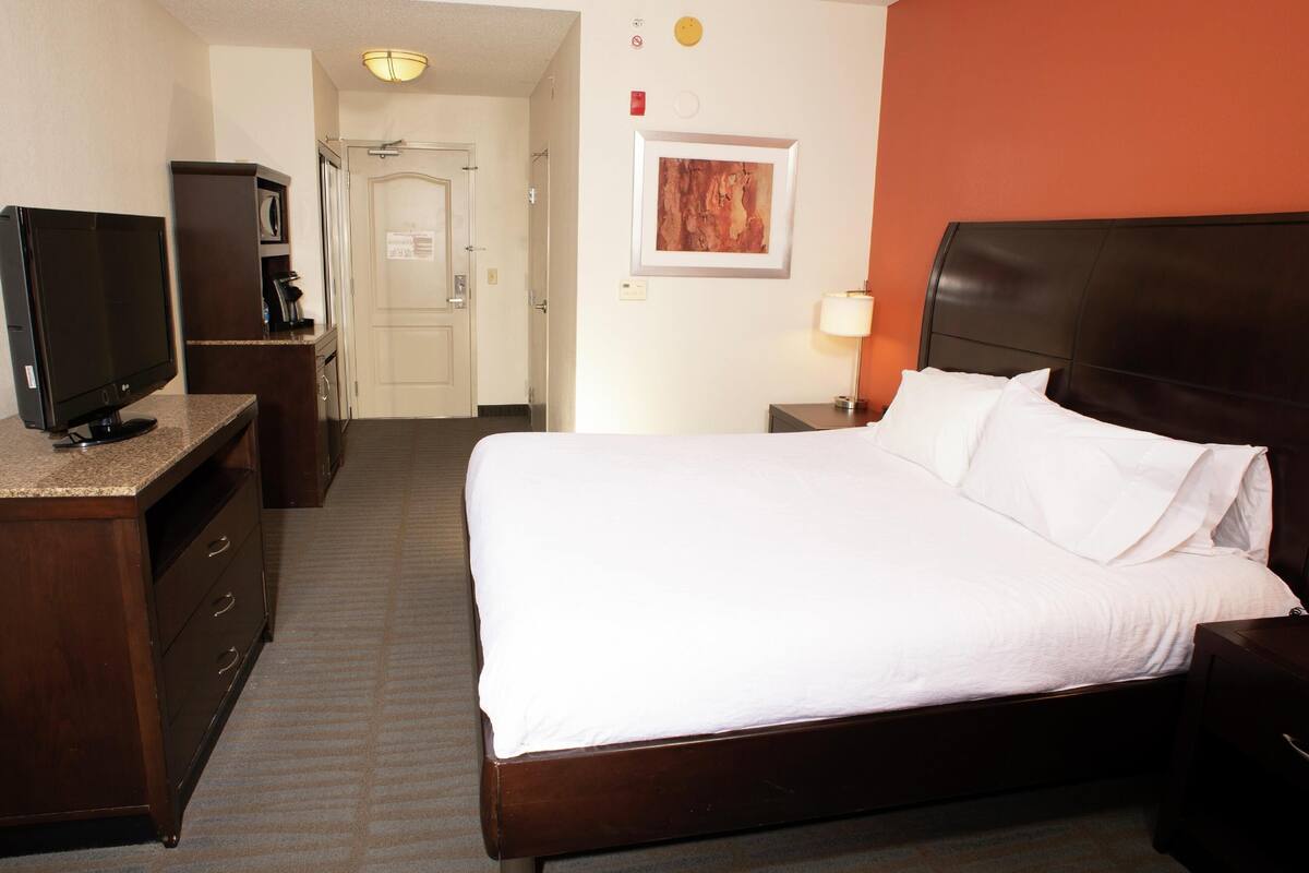 Quarto de hotel com uma cama, televisão, escrivaninha e abajur.