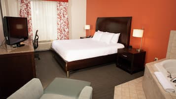 Une chambre d’hôtel comprenant un lit, un bureau avec un ordinateur, une chaise, une table de chevet avec une lampe, et une salle de bain avec une baignoire.