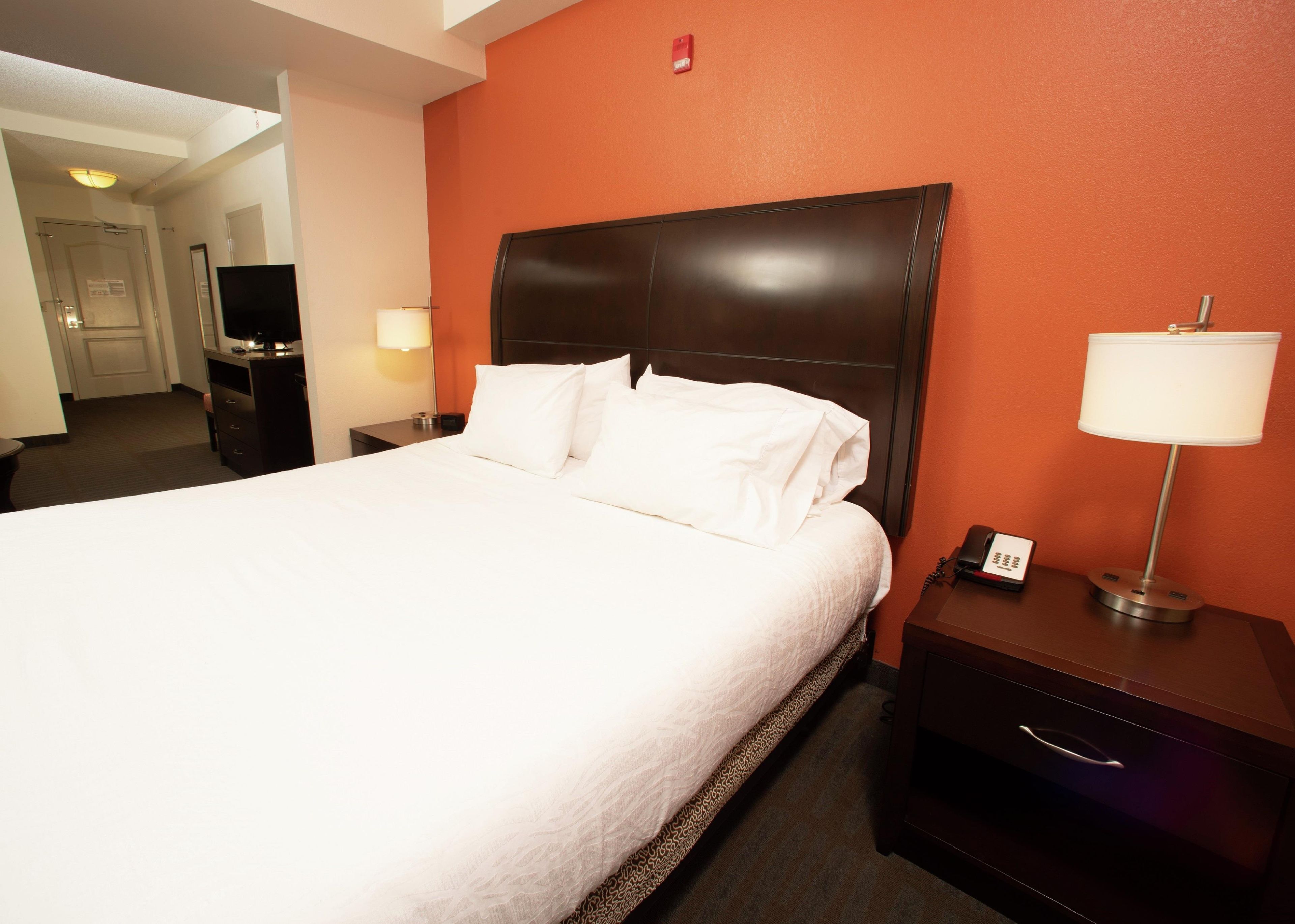 A hotel room with a large bed, a nightstand with a lamp, a TV, and a telephone.