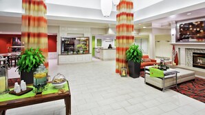 A spacious hotel lobby with a dining area, a fireplace, and a kitchen in the background.
