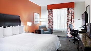A hotel room with a large bed, a desk with a computer, a chair, a TV, and a window with curtains.