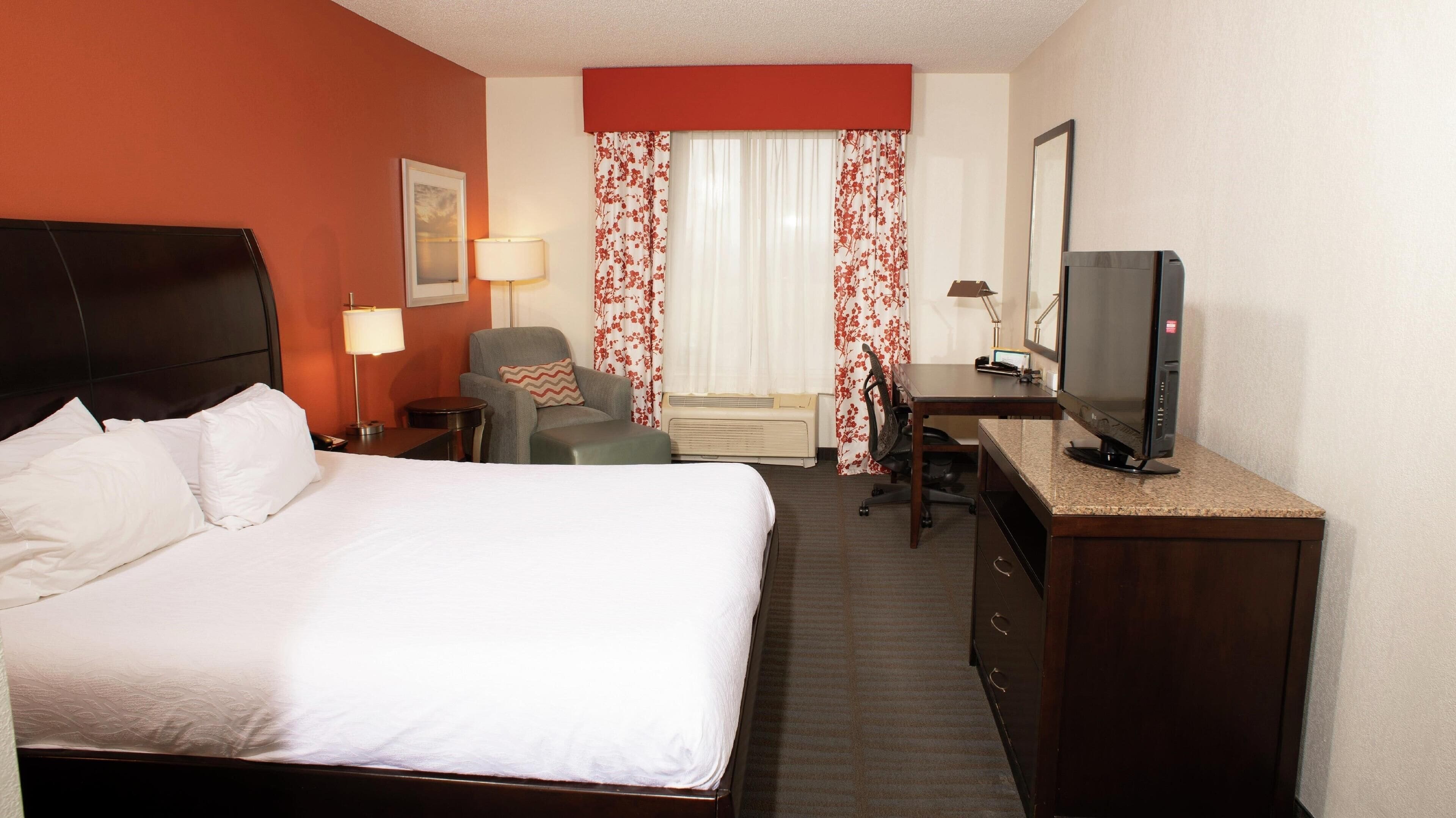 A hotel room with a bed, a desk, a chair, a television, and a window with curtains.