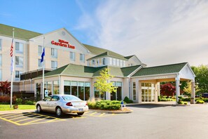 Ein Hilton Garden Inn mit Parkplatz, einer Flagge und blauem Himmel.