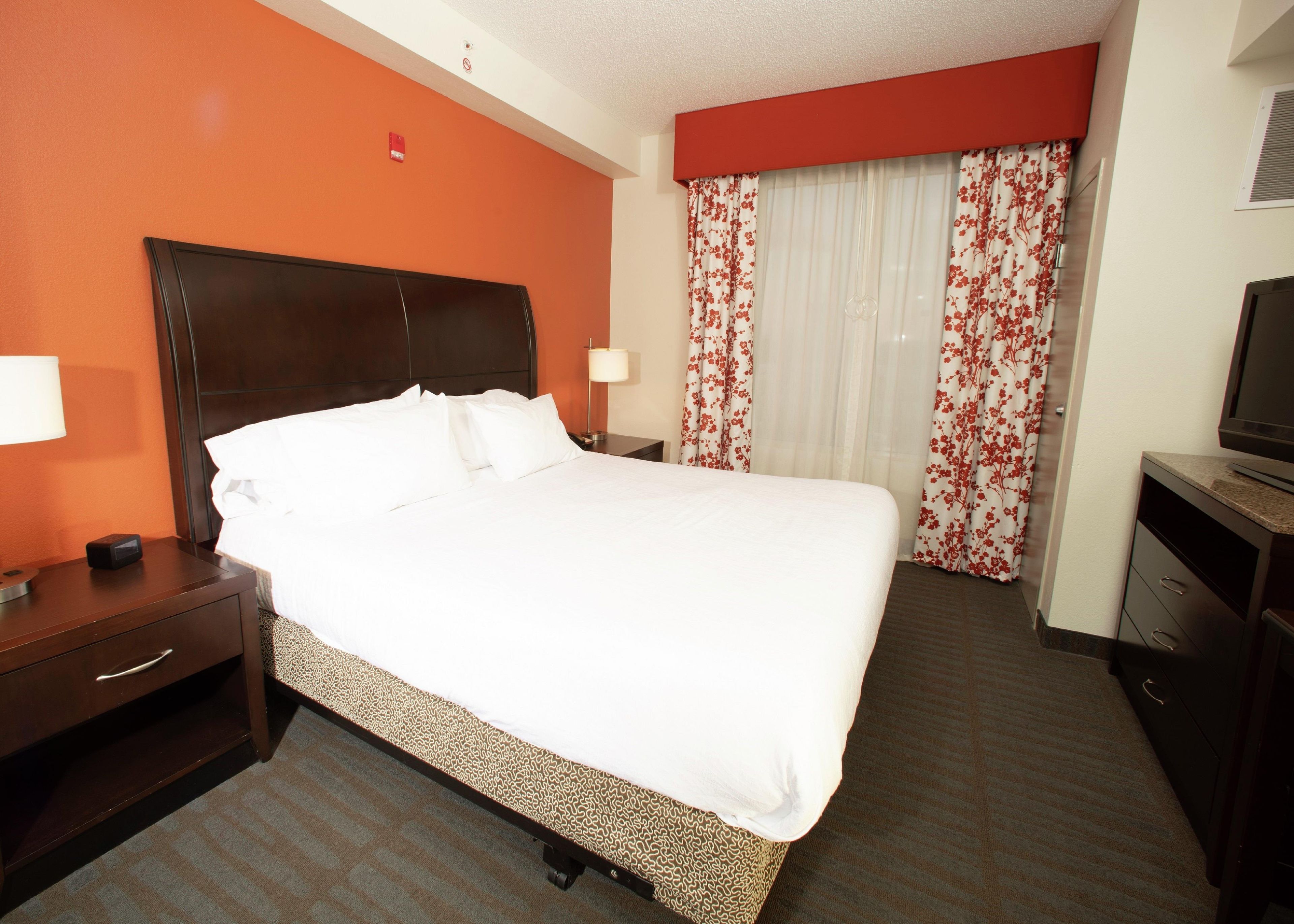 A hotel room with a large bed, a nightstand, a TV, and a window with floral curtains.