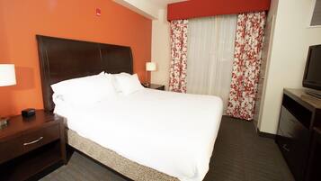 A hotel room with a large bed, a nightstand, a TV, and a window with floral curtains.