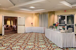 Een feestzaal met een patroon tapijt, witte tafels en een buffetopstelling.