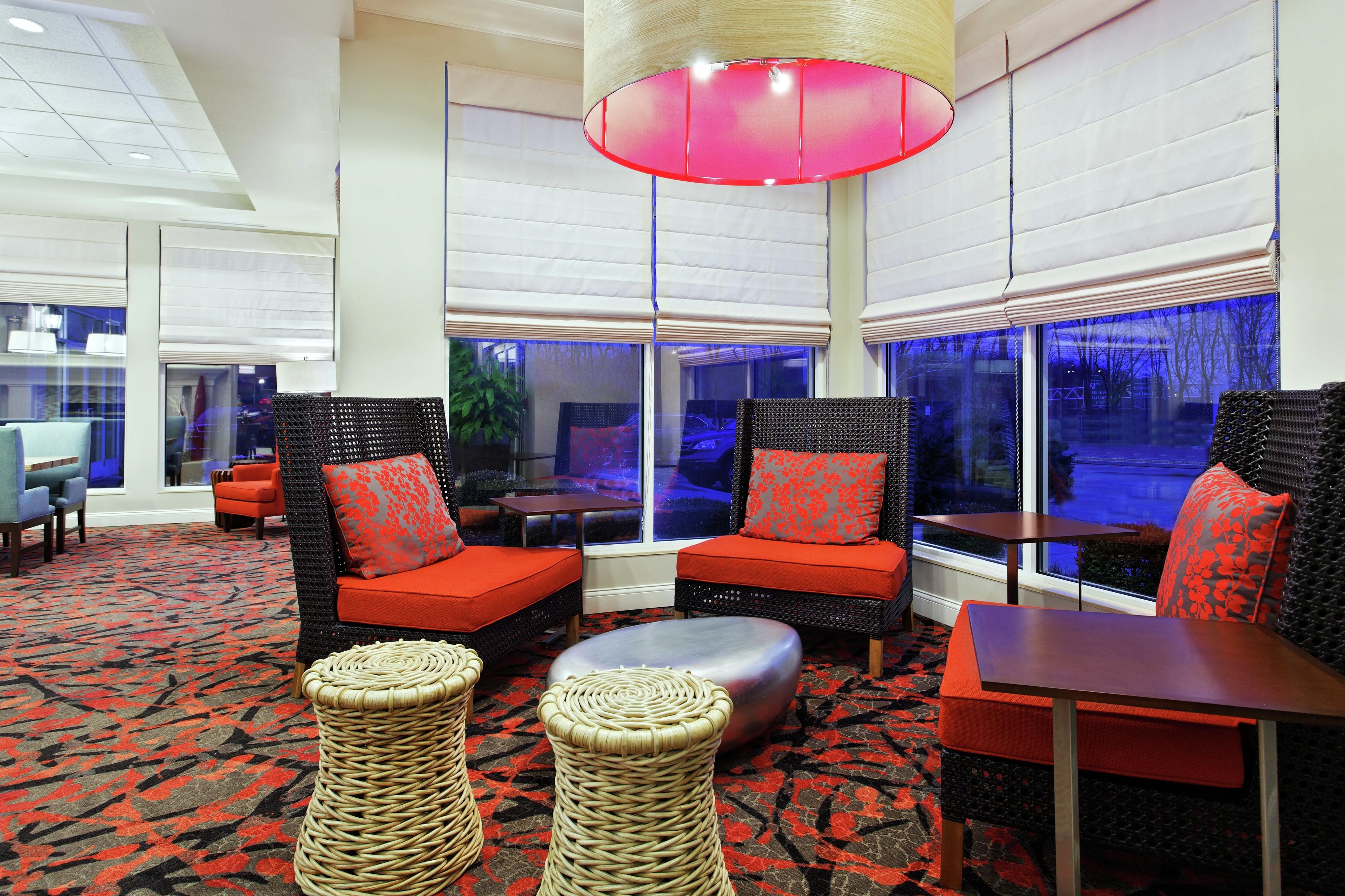 Un área de descanso moderna con muebles de mimbre, cojines rojos y una alfombra estampada.