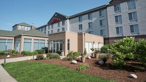 A hotel with a modern design, featuring a mix of residential and commercial spaces. It includes a parking area and landscaped gardens with various plants and rocks.