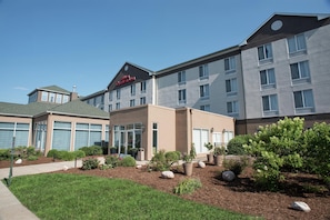 A hotel with a modern design, featuring a mix of residential and commercial spaces. It includes a parking area and landscaped gardens with various plants and rocks.