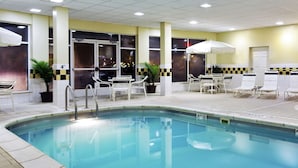 An indoor swimming pool with clear water, surrounded by white lounge chairs and umbrellas.