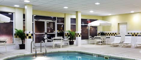 Une piscine intérieure à l’eau claire, entourée de chaises longues blanches et de parasols.