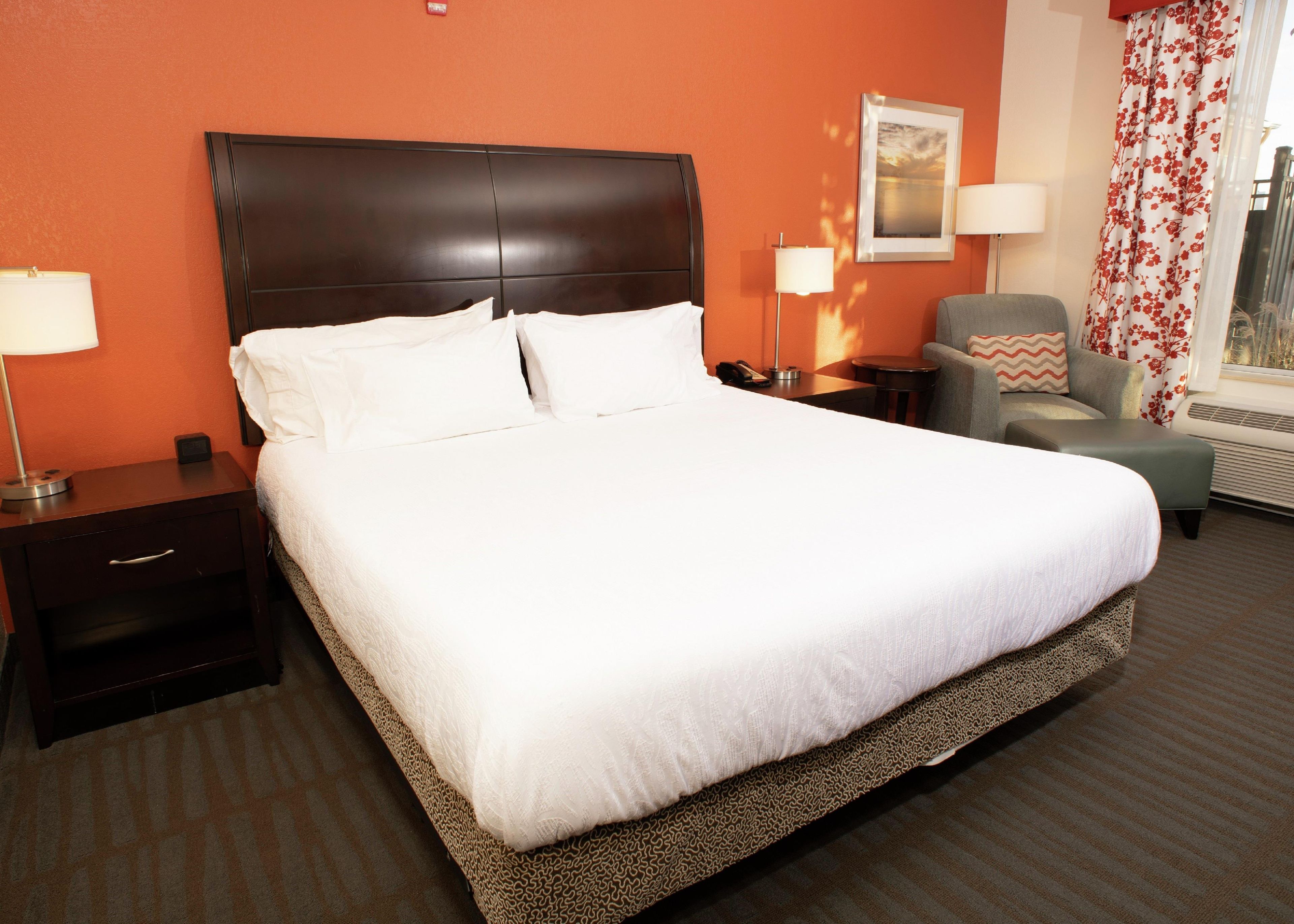 A hotel room with a large bed, two bedside tables, a chair, a lamp, and a picture on the wall.