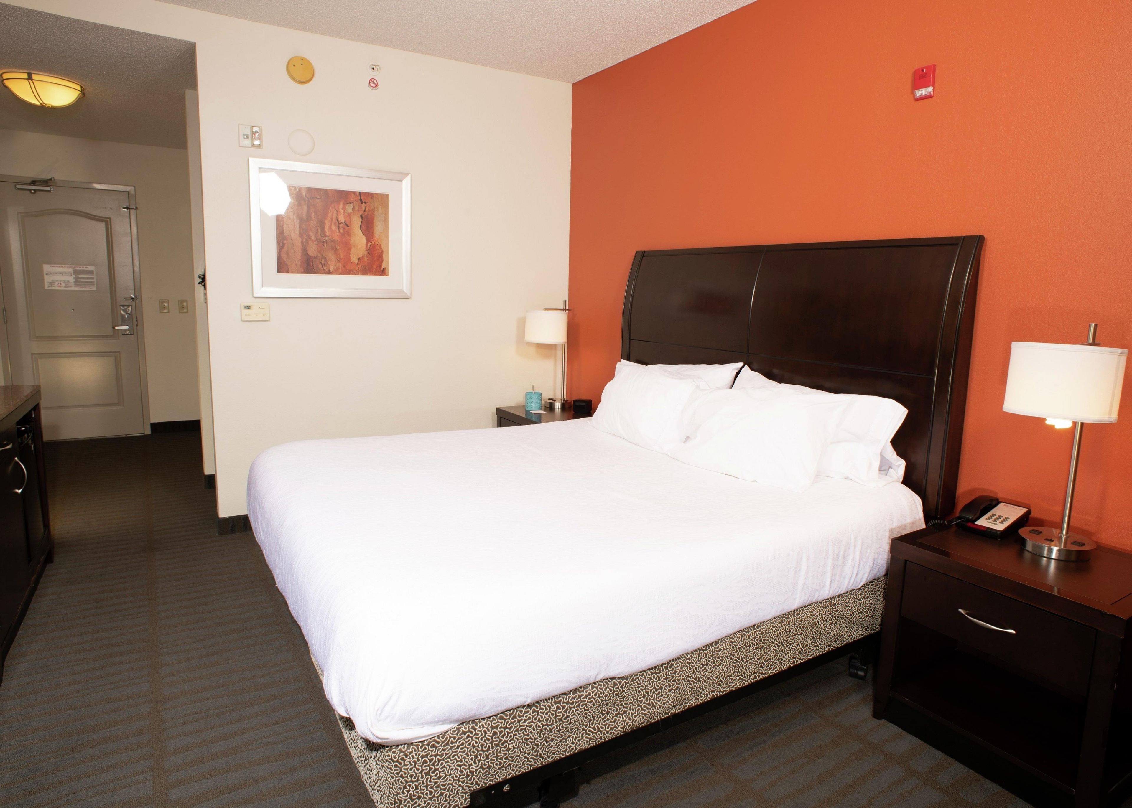A hotel room with a large bed, a bedside table with a lamp, a telephone, and a door leading to another room.